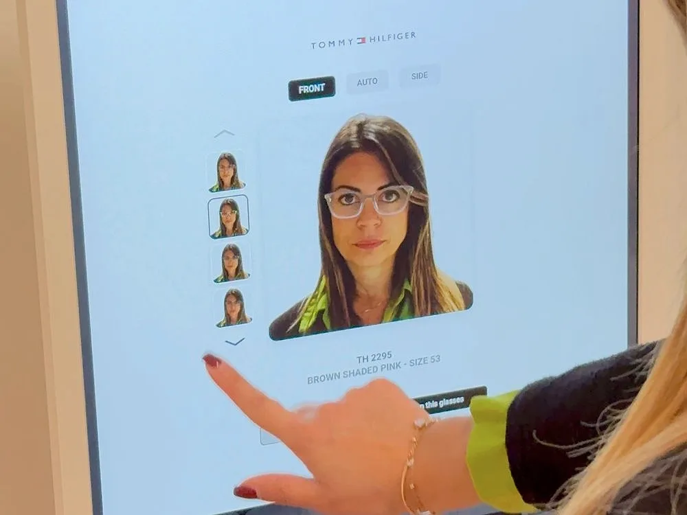 A customer touches the digital mirror: on the screen, her face wearing glasses and, alongside, the same face in other frames.