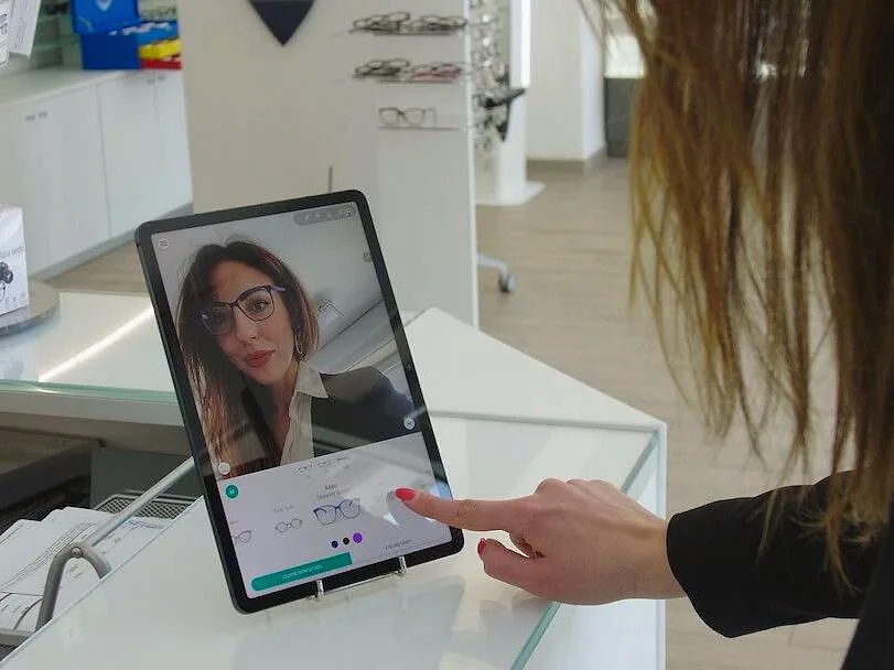 A tablet on an optician's counter: a customer sees herself wearing the glasses and chooses the frame on the screen.