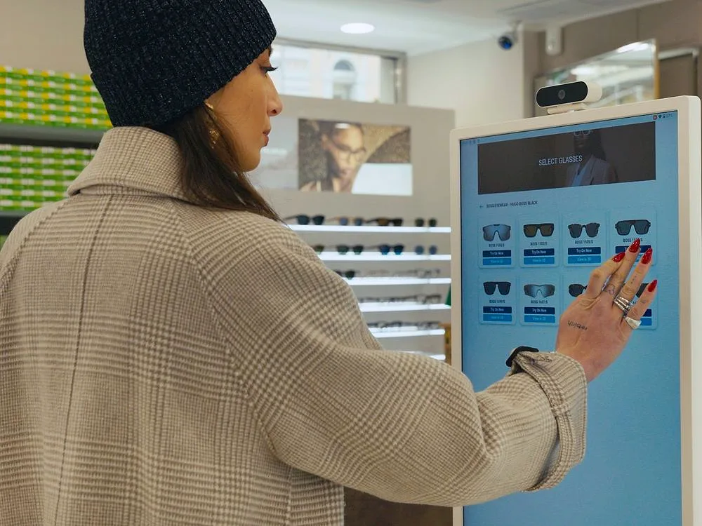 In an optician's shop, a customer chooses sunglasses by tapping the frames on the digital mirror's screen.