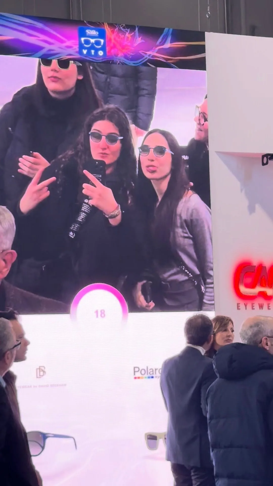 A giant screen at a trade fair: three young women see themselves in virtual sunglasses and pose for the photo.