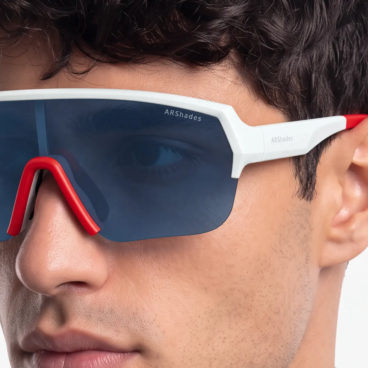 Primo piano di un occhiale sportivo a mascherina Airstorm indossato: montatura bianca con ponte rosso e lente blu specchiata, la scritta ARShades sulla lente e sull'asta nitida e leggibile.